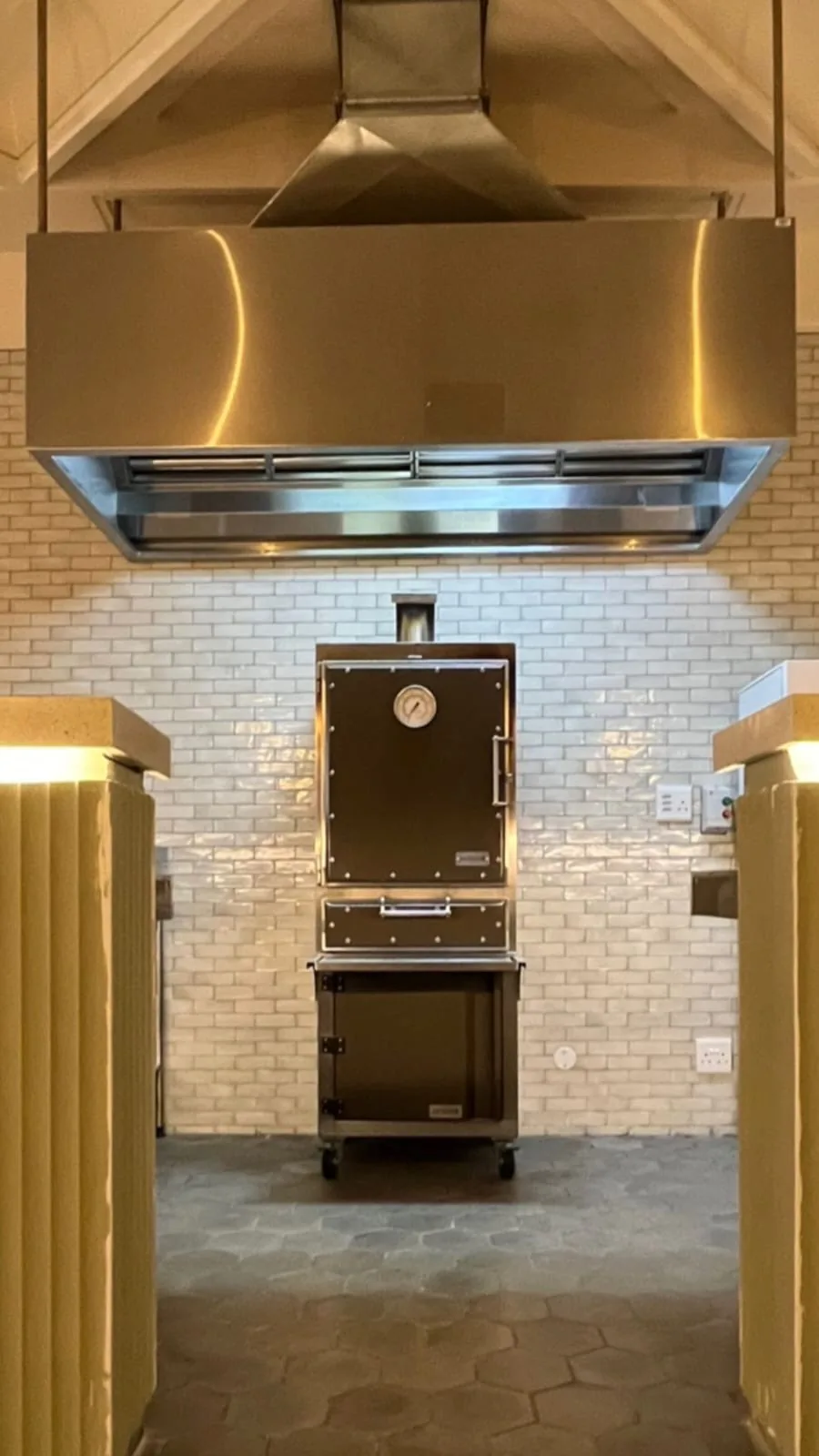 A black Inferno charcoal oven in a white-tiled alcove under its own extraction hood.