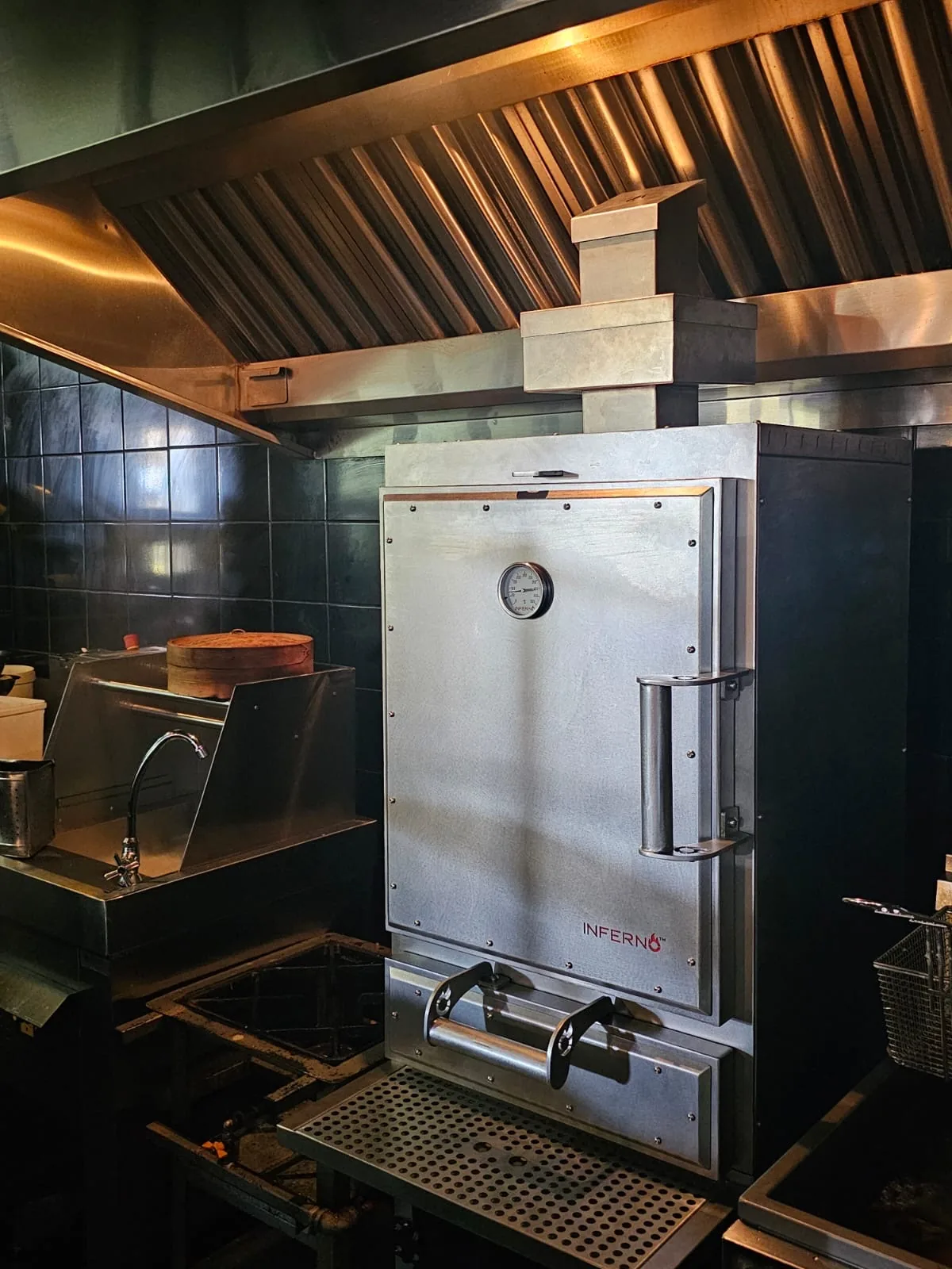 An Inferno charcoal oven with a stainless door, installed under the extraction hood of a commercial kitchen.