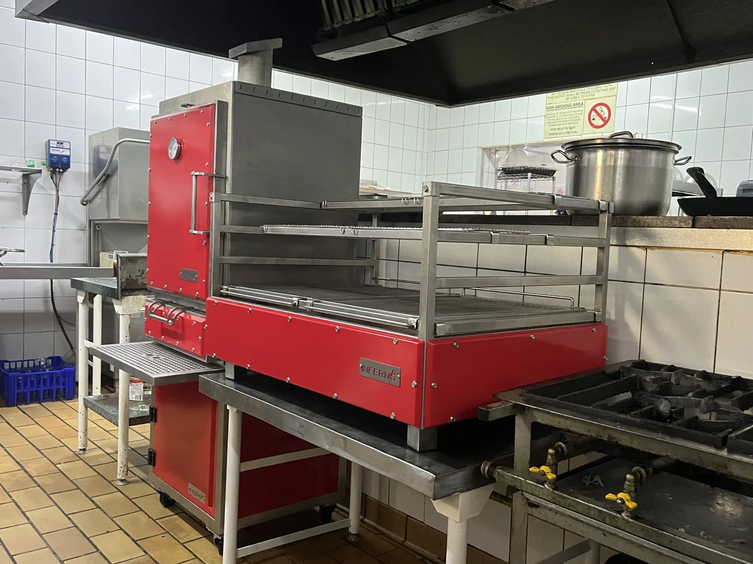 A red Inferno charcoal oven with a red grill in a tiled commercial kitchen.