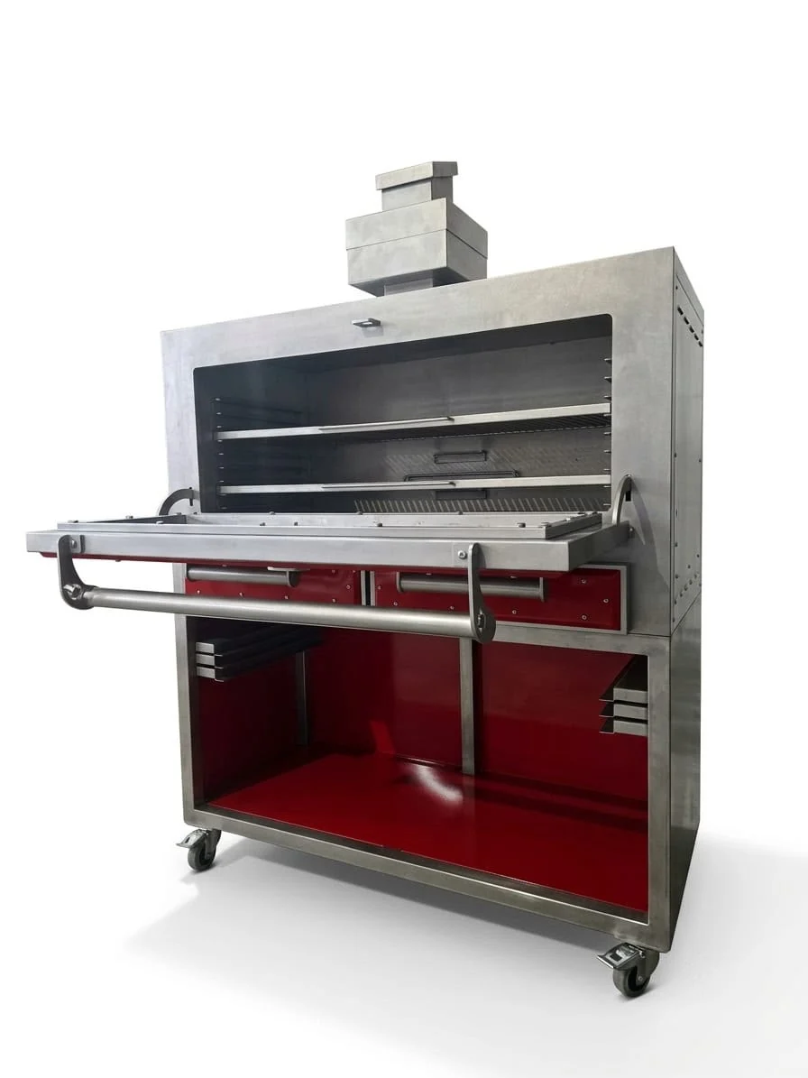 The Inferno 1200 from the front right with its door folded down, showing rod grids on runners across the wide stainless chamber, two red drawers below and the stepped chimney on top.