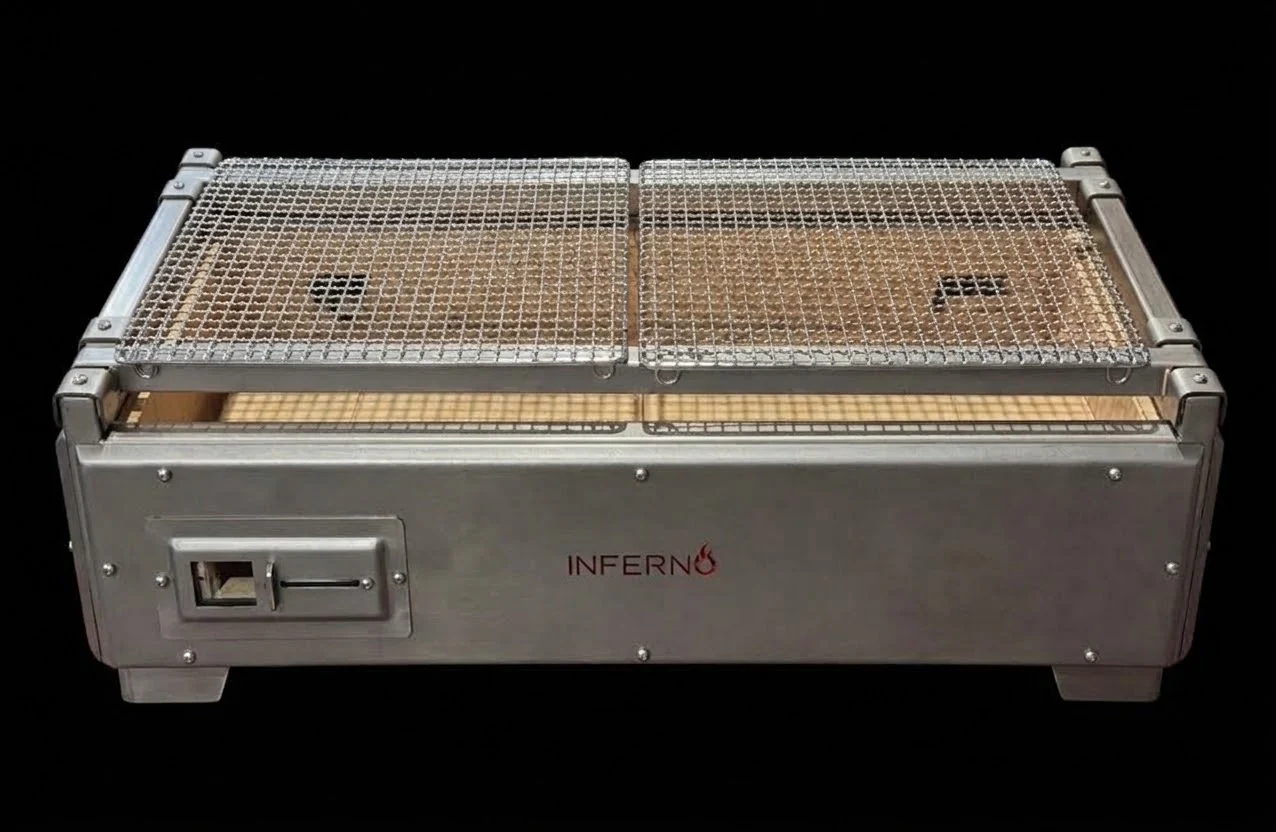 The Yakitori Grill from the front: the stainless-steel body with a sliding damper vent at the left and the Inferno logo at the right, two mesh grates across the top, on short feet, on a black ground.